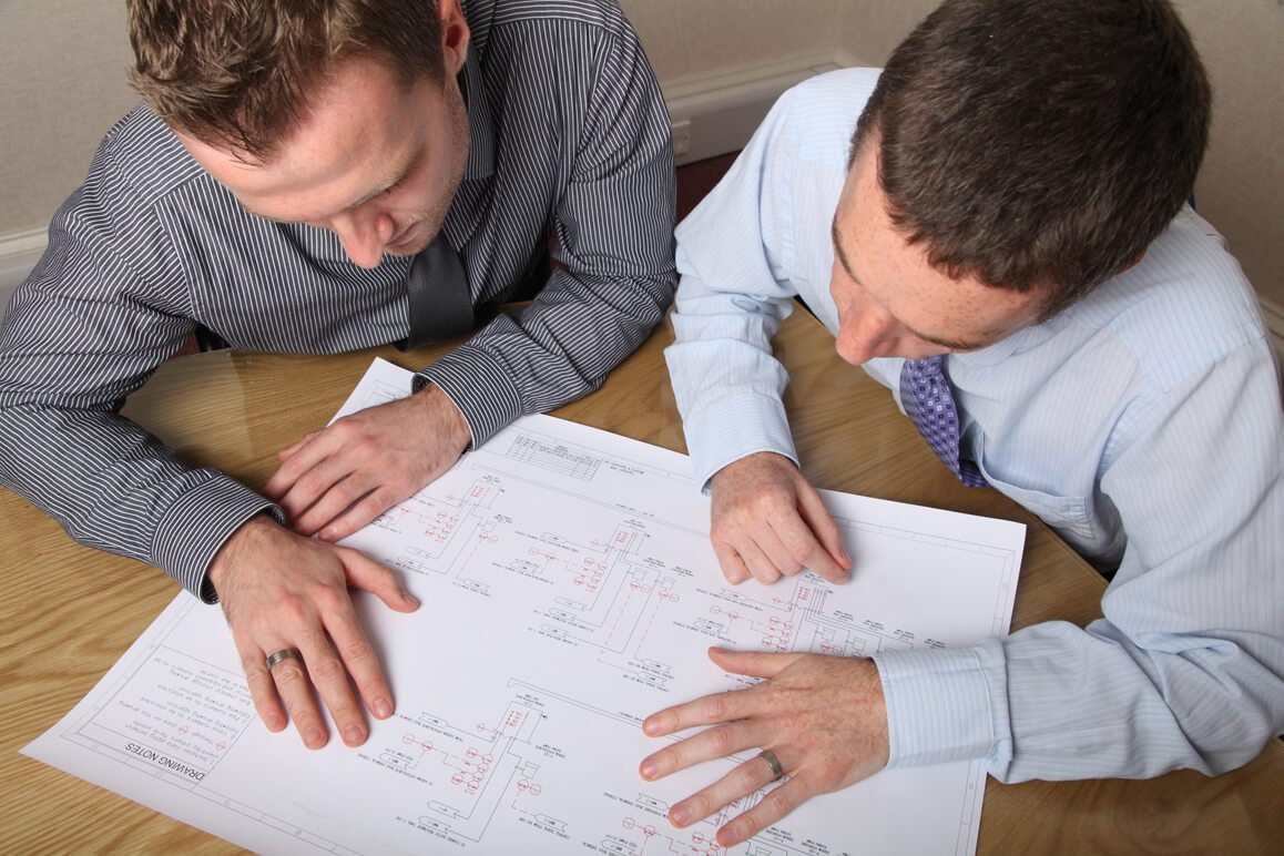 Two men looking at blueprints at a table.