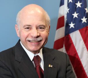 A man in a suit and tie standing in front of an american flag.