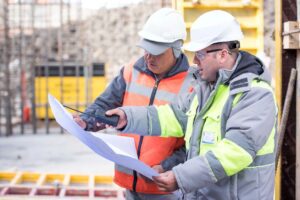 Two construction workers looking at blueprints on a construction site.