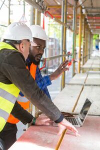 Two construction workers looking at a laptop on a construction site.